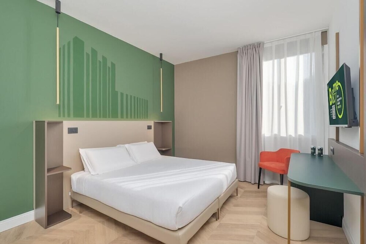 A hotel room with a bed, a desk, a chair, a TV, and a window with curtains.