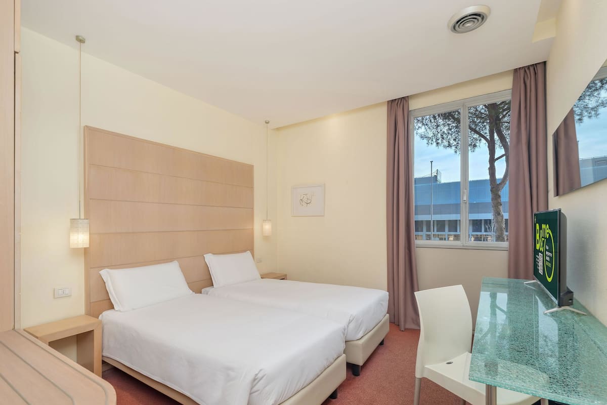 A hotel room with a double bed, a desk with a glass top, and a window with curtains.