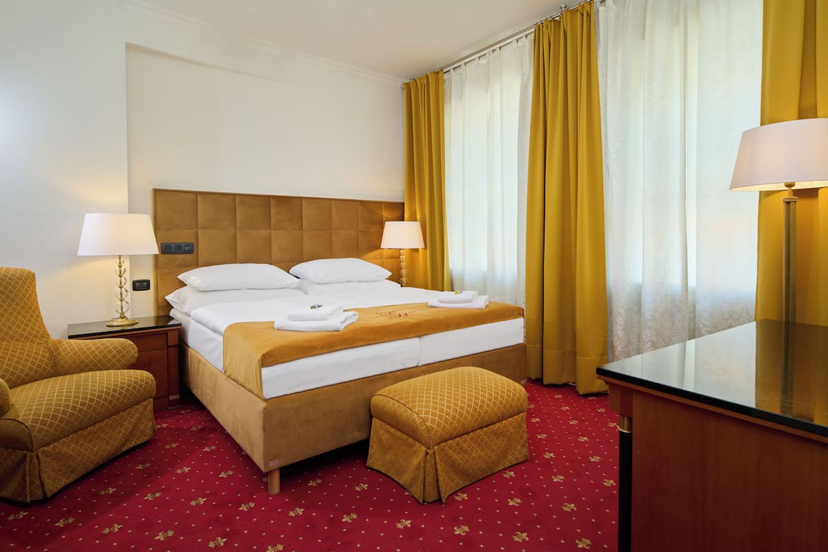 Habitación de hotel con una cama grande, dos mesitas de noche con lámparas, un escritorio de madera, una silla y piso cubierto con alfombra roja.