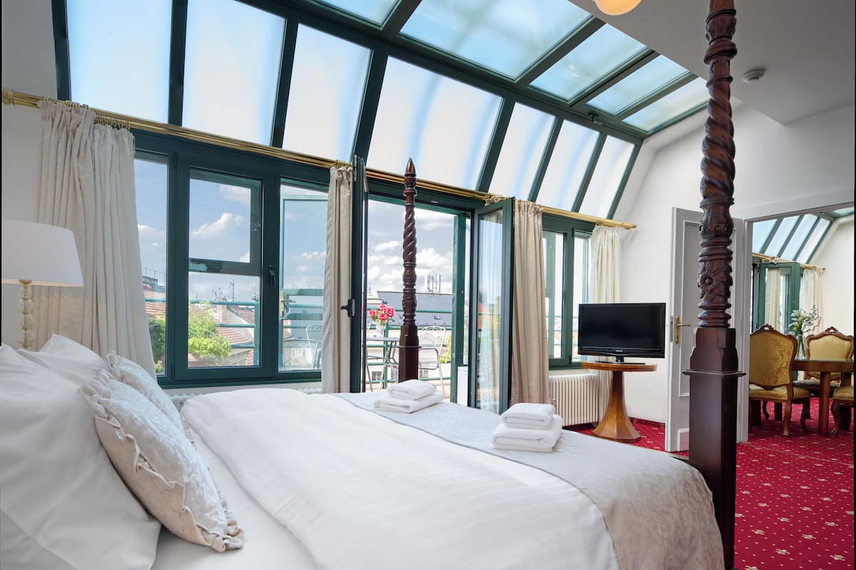 Habitación de hotel con una cama grande, un televisor, una silla de madera y vistas a través de un tragaluz.