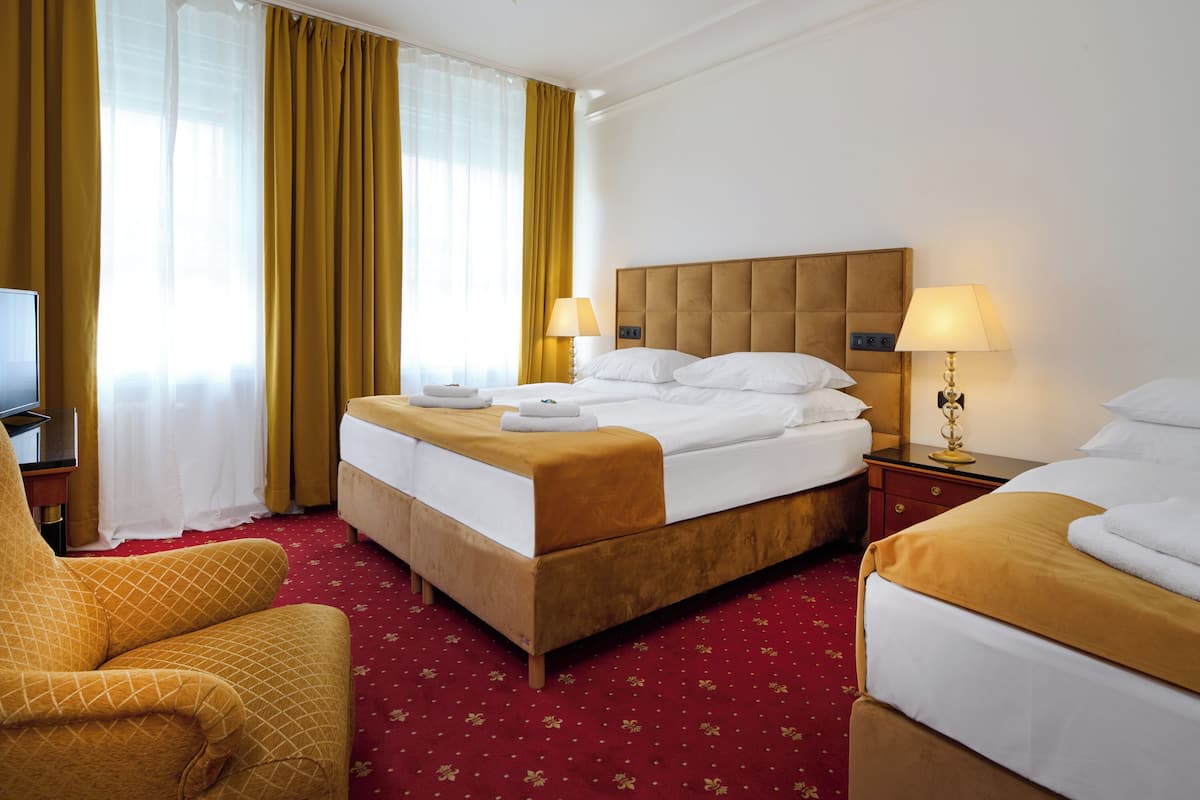 Habitación de hotel con una cama grande, dos mesitas de noche, una silla, un televisor y una ventana con cortinas.