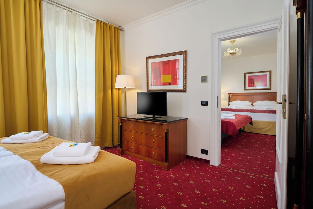 Habitación de hotel con dos camas, televisión, cómoda y piso cubierto de alfombra roja.