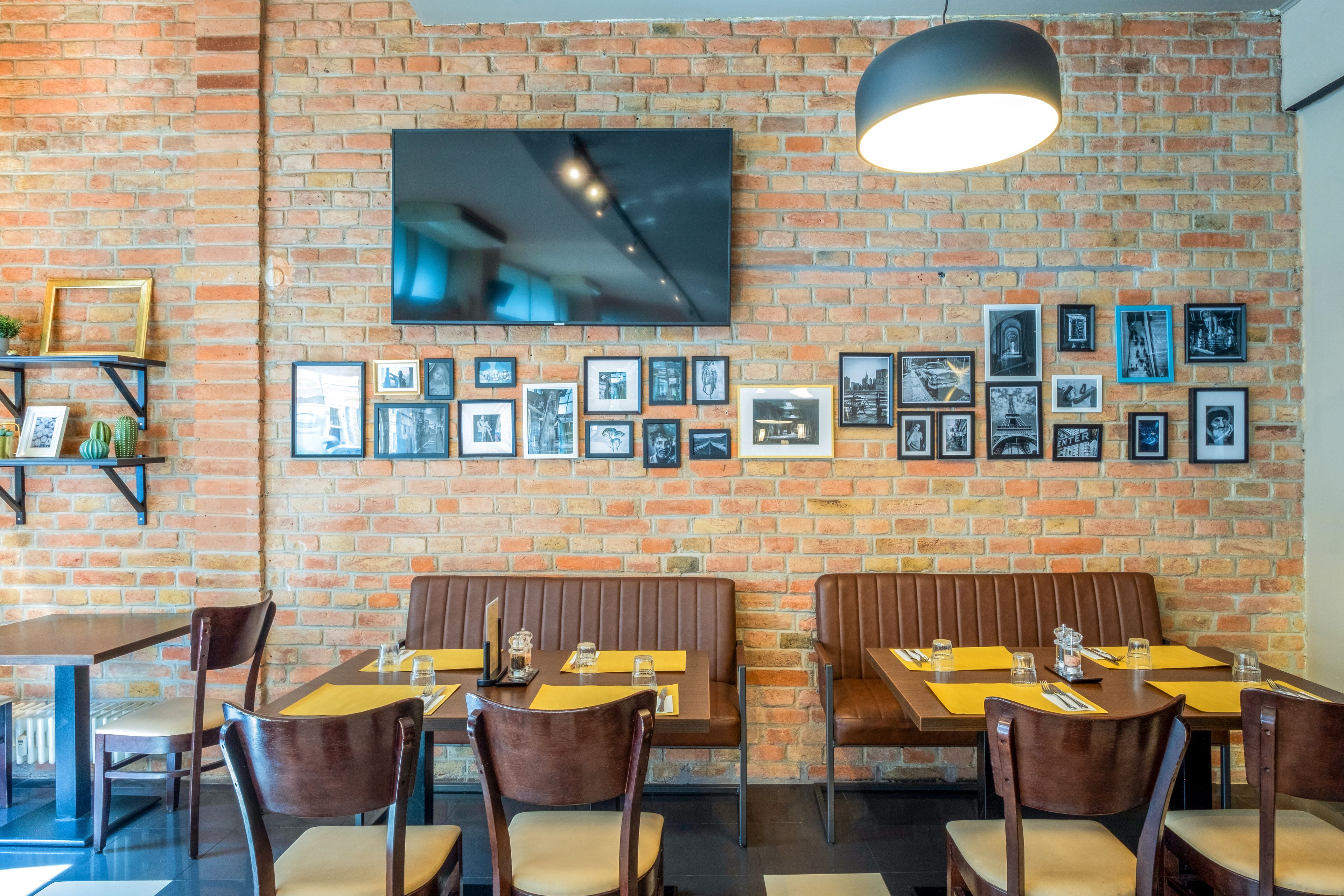 A restaurant with brick walls, a flat-screen TV, framed pictures, wooden tables, and cushioned chairs.