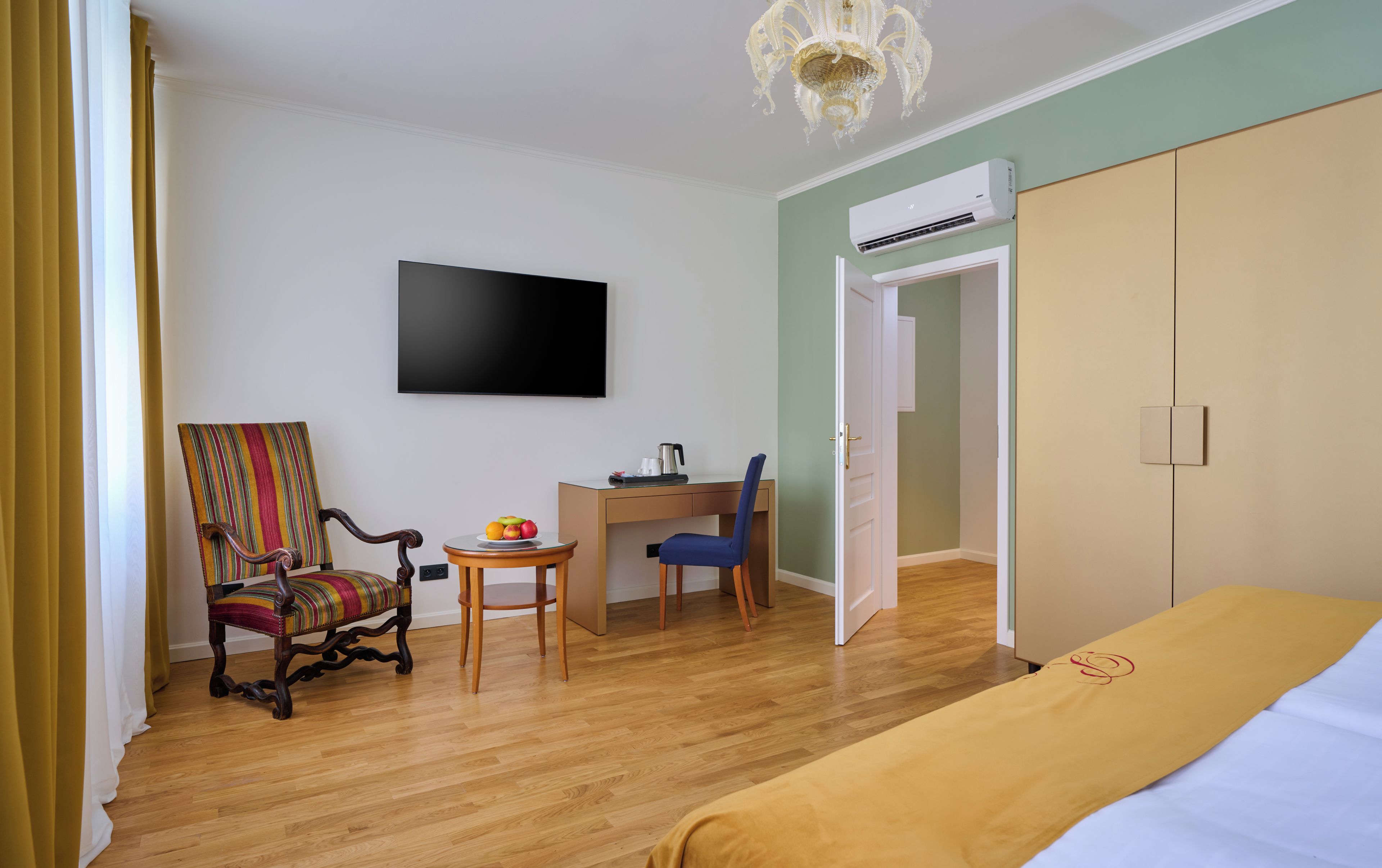 A hotel room with a bed, a desk with a chair, a television, and an air conditioning unit.