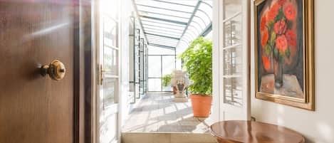 Un couloir avec une porte en bois, une plante en pot, une table et un tableau accroché au mur.