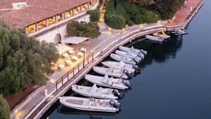 Une propriété située au bord de l’eau, avec une rangée de bateaux amarrés, un bâtiment doté d’un toit recouvert de tuiles rouges et une promenade pavée longeant le rivage.