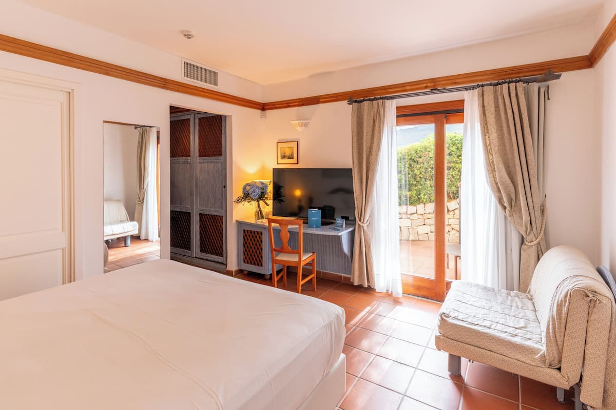 Un dormitorio con cama, escritorio, silla, televisor y vistas al exterior.