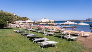 Une zone de plage aménagée avec de nombreux transats et parasols, un ciel bleu dégagé et une vue sur la mer.