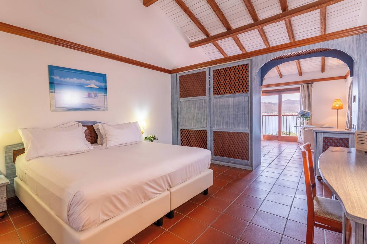 Una habitación de hotel con cama, una mesa de comedor, un balcón con vistas y techo de madera.