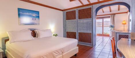 A hotel room with a bed, a dining table, a balcony with a view, and a wooden ceiling.