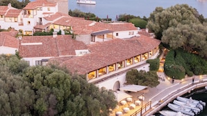 Un bâtiment situé sur la côte, doté d’une terrasse donnant sur la mer, d’un quai avec des bateaux et d’un chemin menant à l’entrée.