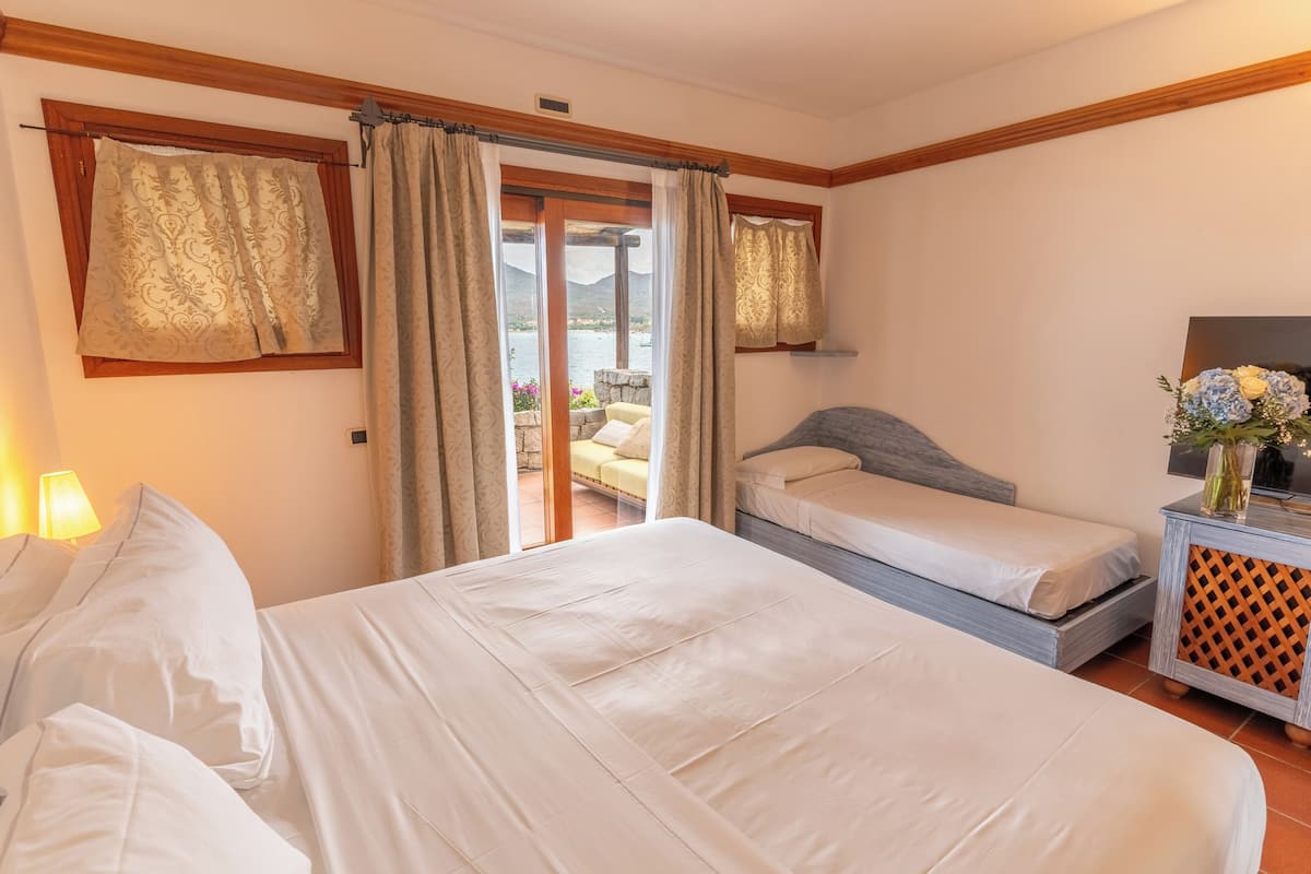 Un dormitorio con dos camas, un sofá, una mesita con un florero y vistas a un balcón con mobiliario exterior.