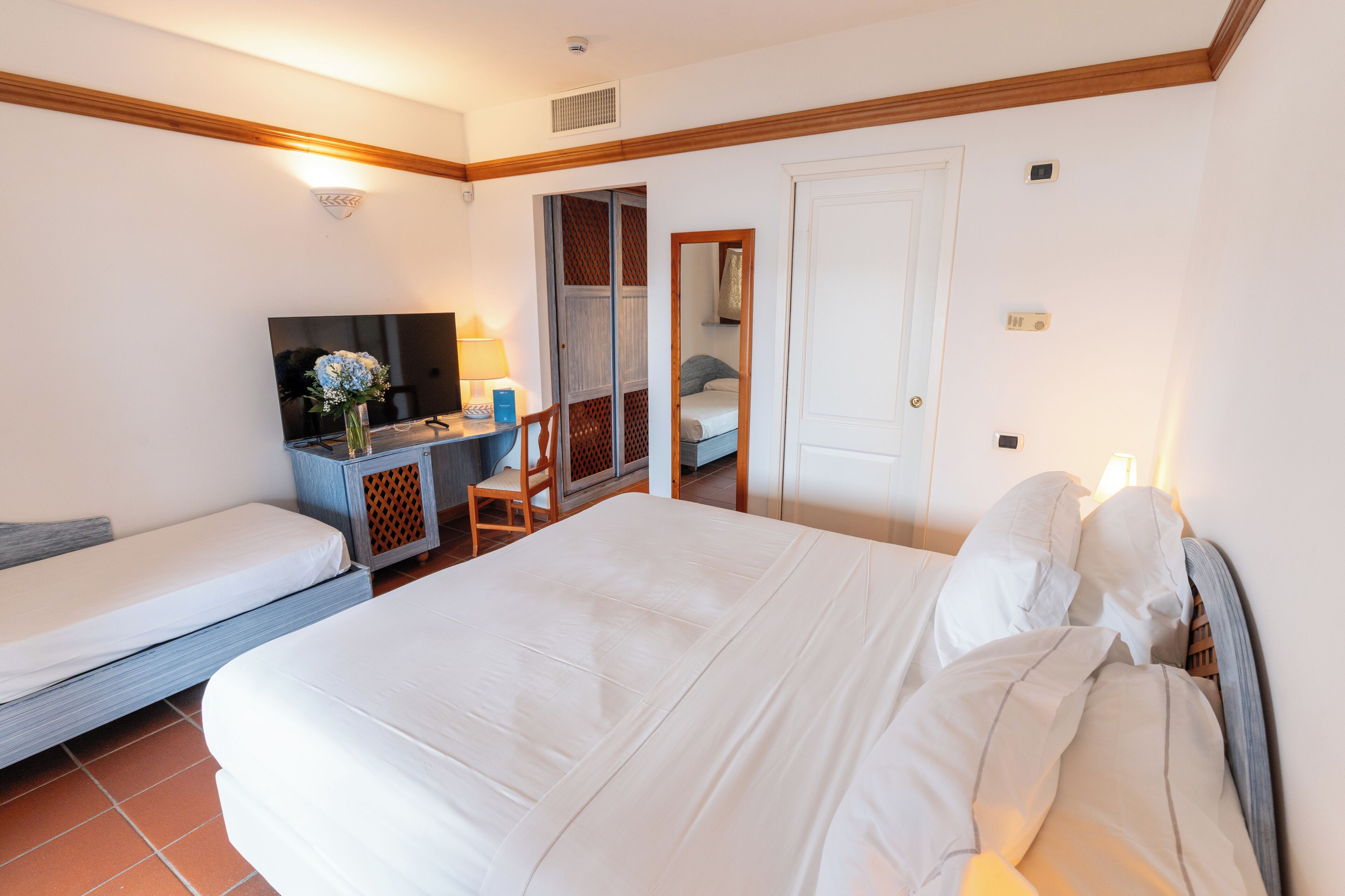 Hotellihuone, jossa on suuri sänky, työpöytä tuolilla, televisio ja vaatekaappi.