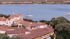 Une ville côtière avec des bâtiments, une marina où sont amarrés des voiliers, et un paysage montagneux en arrière-plan.