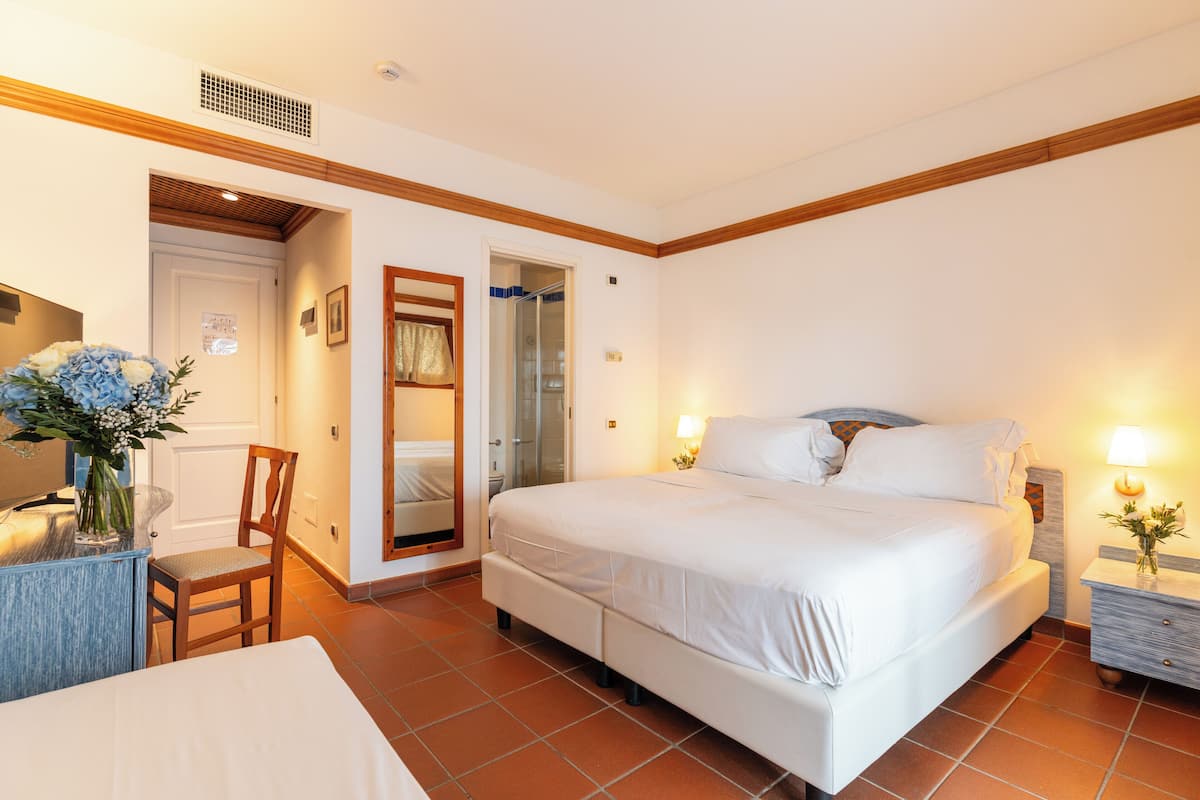 Una habitación de hotel con cama, una silla, escritorio, espejo y puerta que da a un baño.