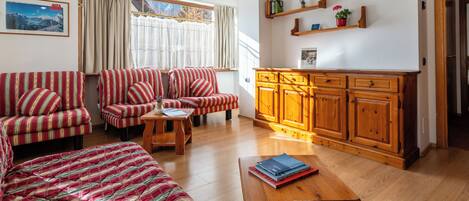 Una sala de estar con sofás a rayas, una mesa de centro de madera y una zona de cocina con armarios y estantes de madera.