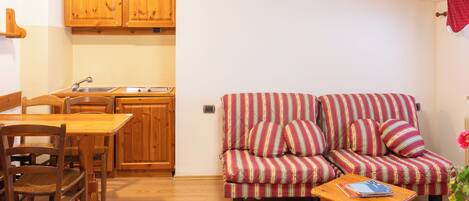 Un espacio habitable compacto con kitchenette, un sofá a rayas, una mesa de comedor de madera y una pequeña mesita de noche de madera.