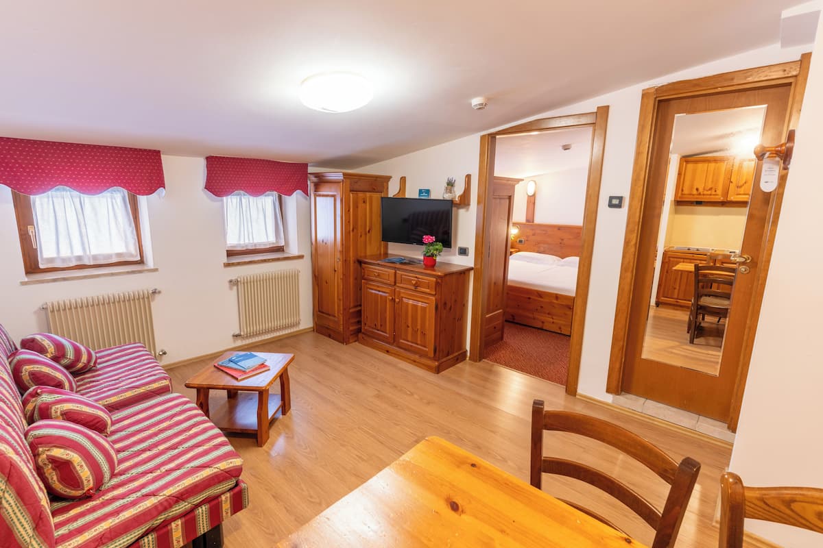 Una habitación compacta con sofá, una mesita, televisor, un armario de madera y una cama.
