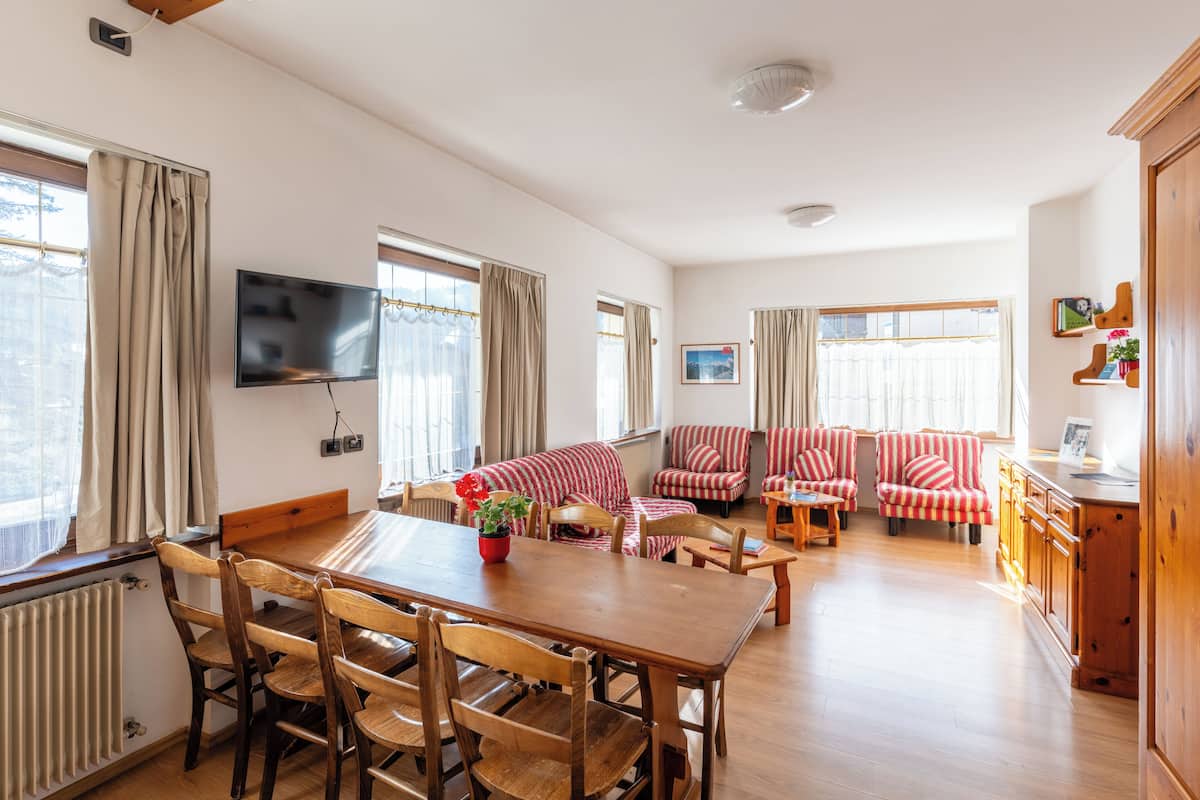 Un amplio salón con mesa y sillas de madera, un conjunto de sofás y un televisor montado en la pared.