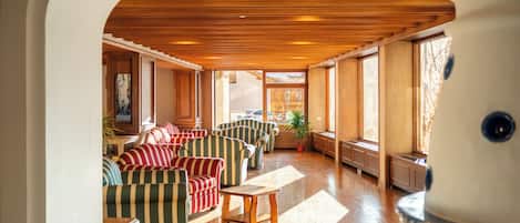 A spacious room with wooden flooring, striped sofas, a wooden table, and large windows.