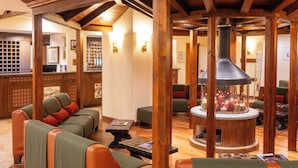 A cozy lobby with wooden beams, a central fireplace, and seating areas.