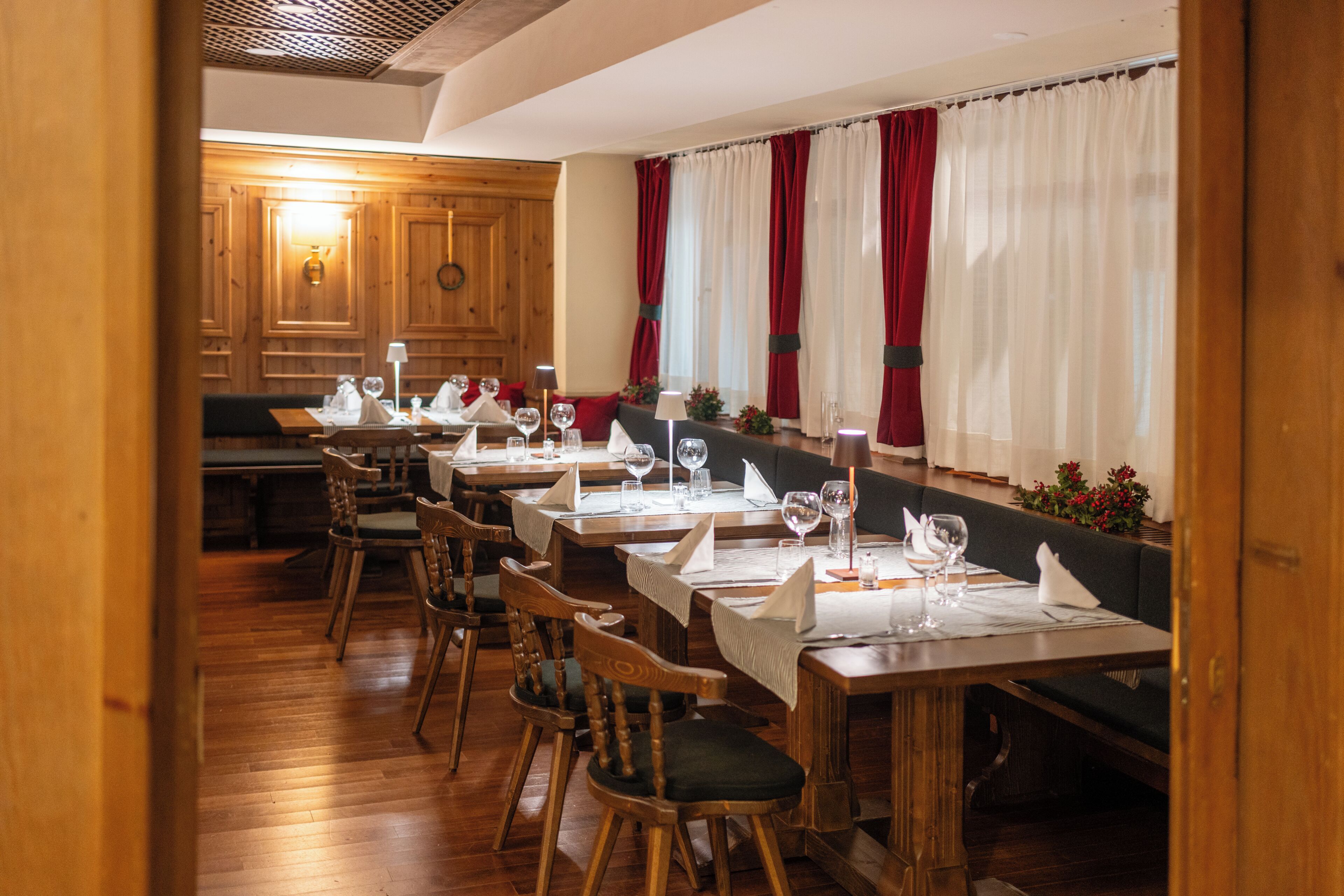 A restaurant with wooden tables and chairs, red and white curtains, and a wooden ceiling.