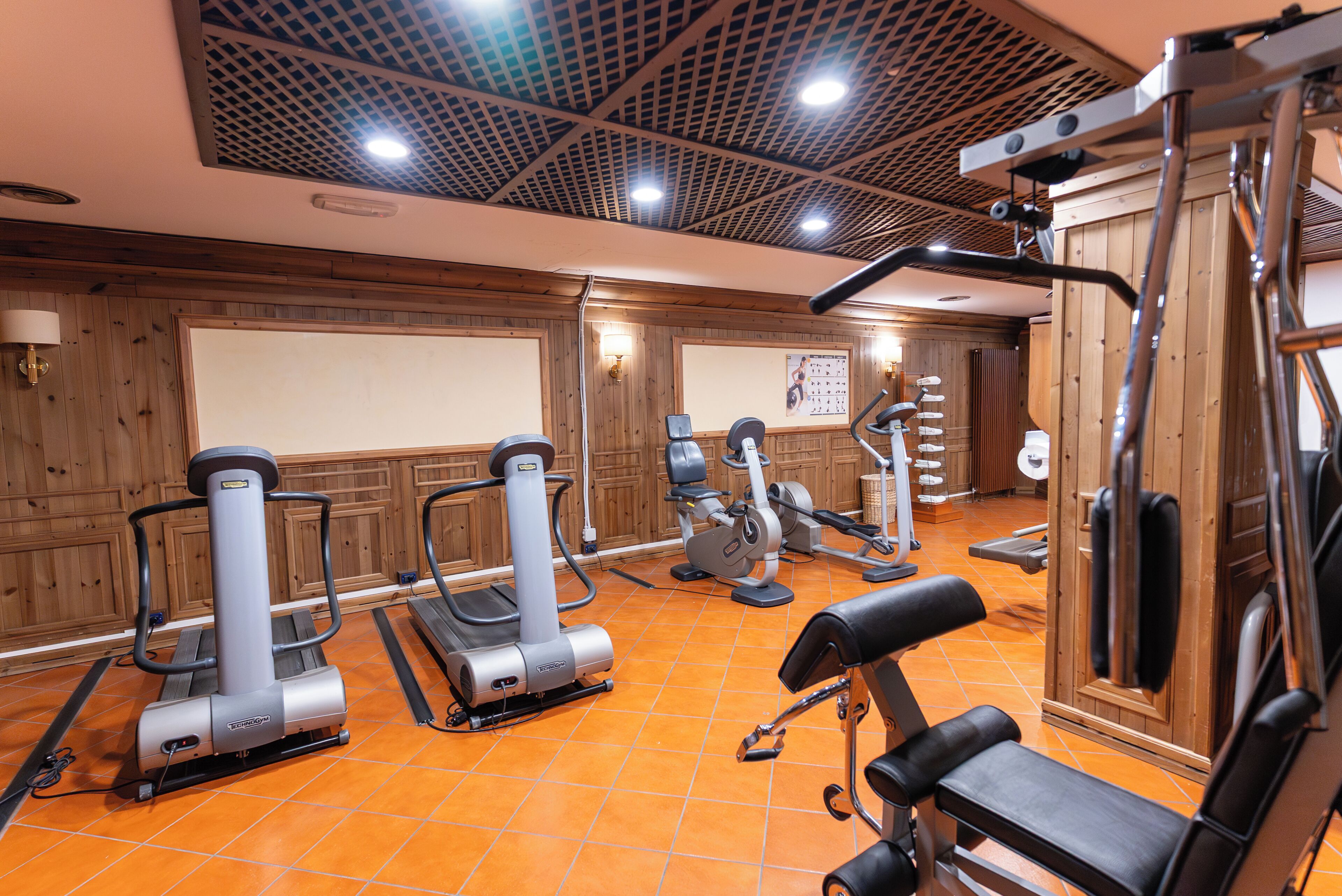 Un gimnasio con máquinas de ejercicio, un televisor montado en la pared y paneles de madera.