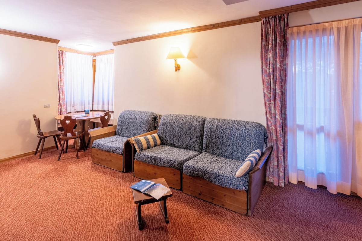 Una habitación amoblada con sofá, una mesita, una silla, una lámpara y una ventana con cortinas.