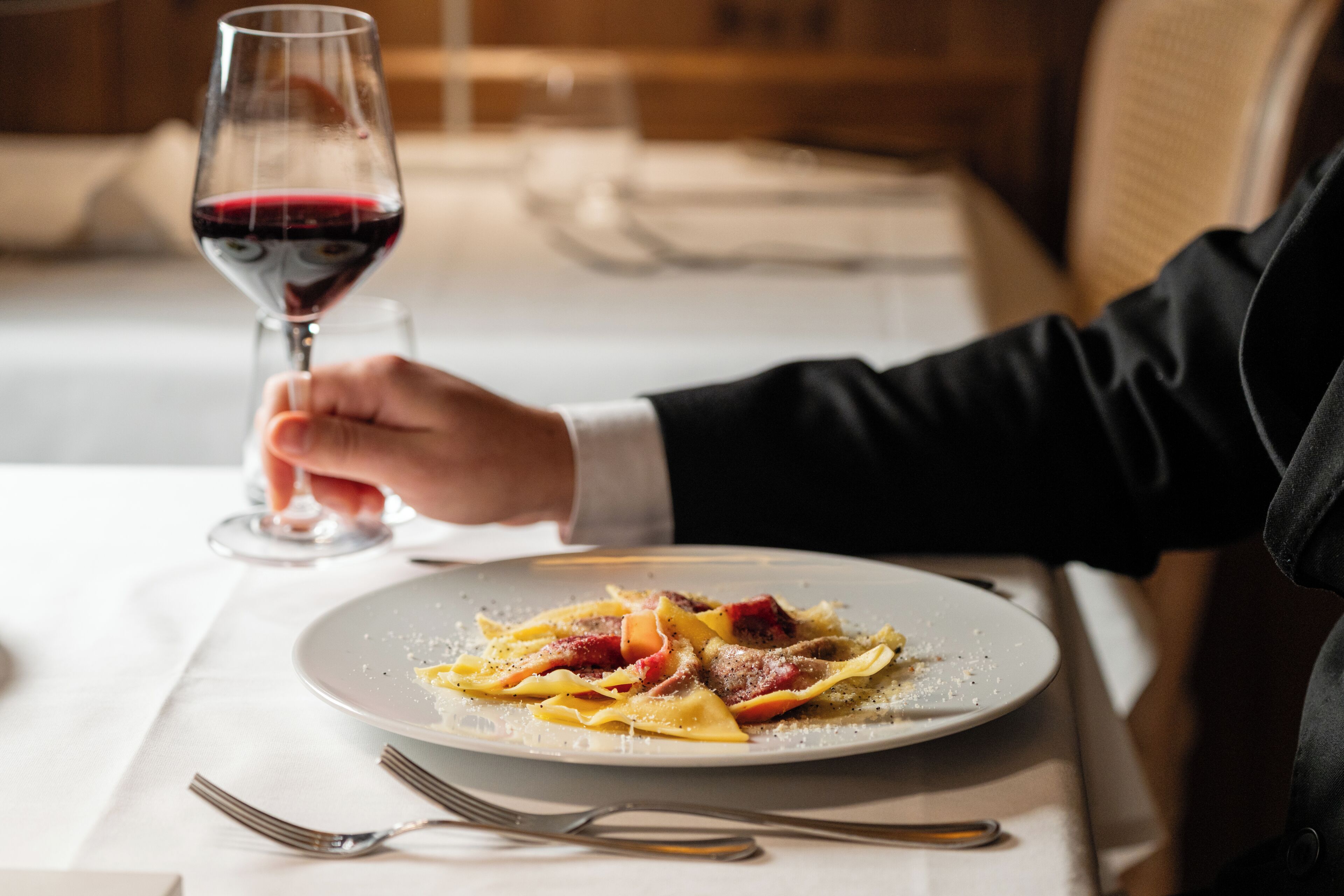 Une table à manger avec une assiette de pâtes, un verre de vin rouge et des couverts.
