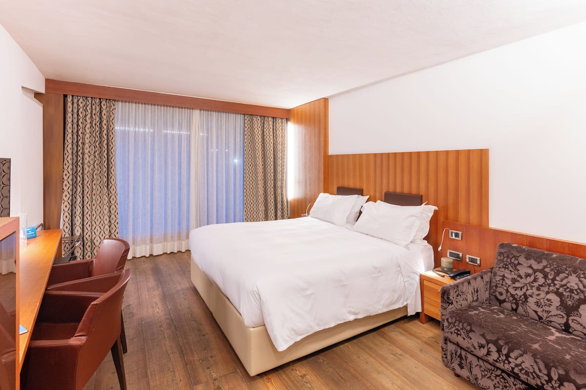 Una habitación de hotel con una cama, un escritorio, una silla, una mesita de noche y un sofá estampado.