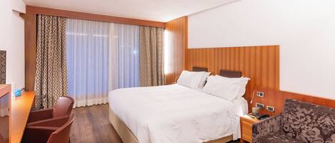 Ein Hotelzimmer mit Bett, Schreibtisch, Stuhl, Nachttisch und einer gemusterten Couch.