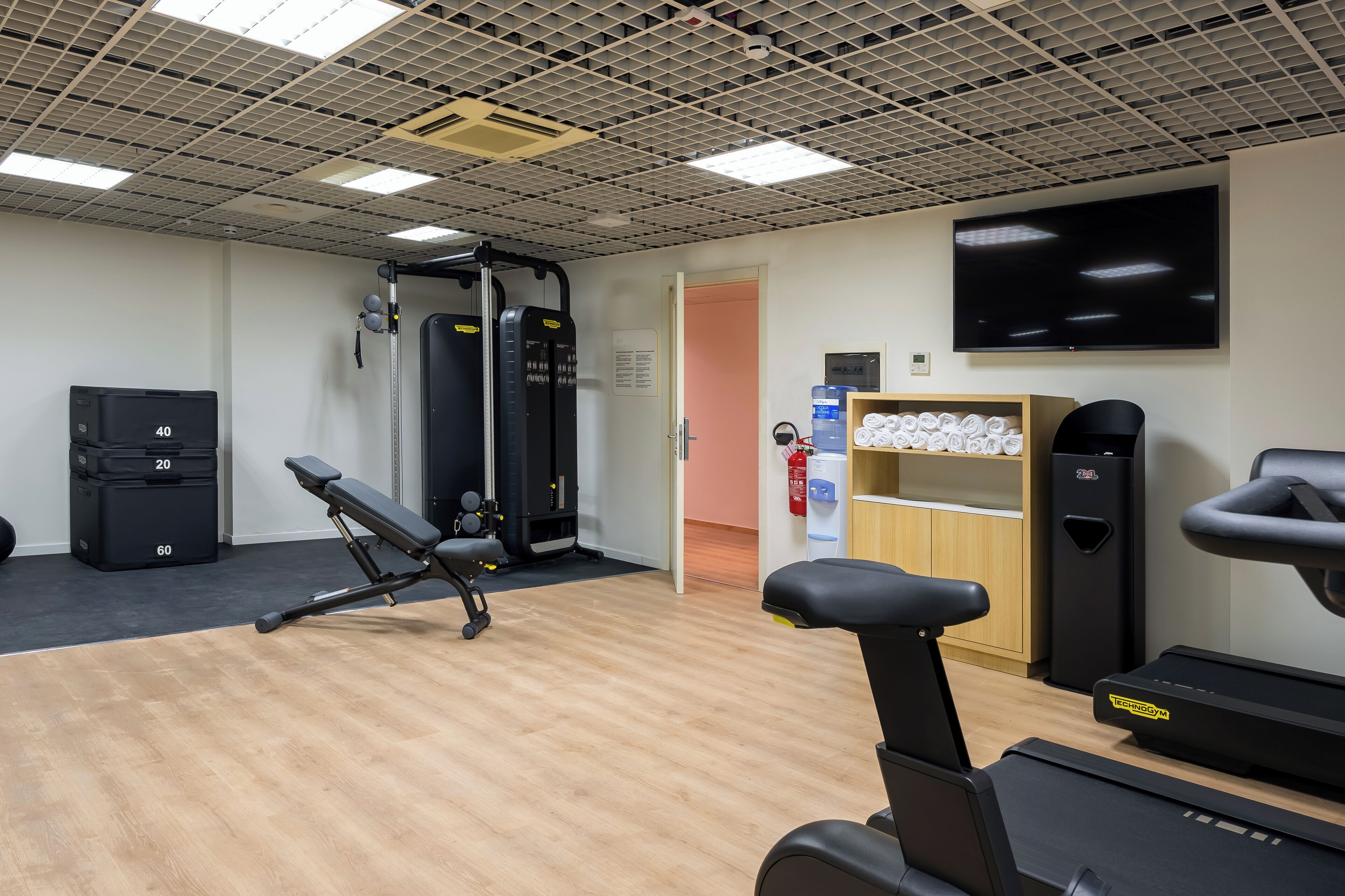 Une salle de sport équipée de matériel d’exercice, d’un tapis de course et d’un téléviseur fixé au mur.