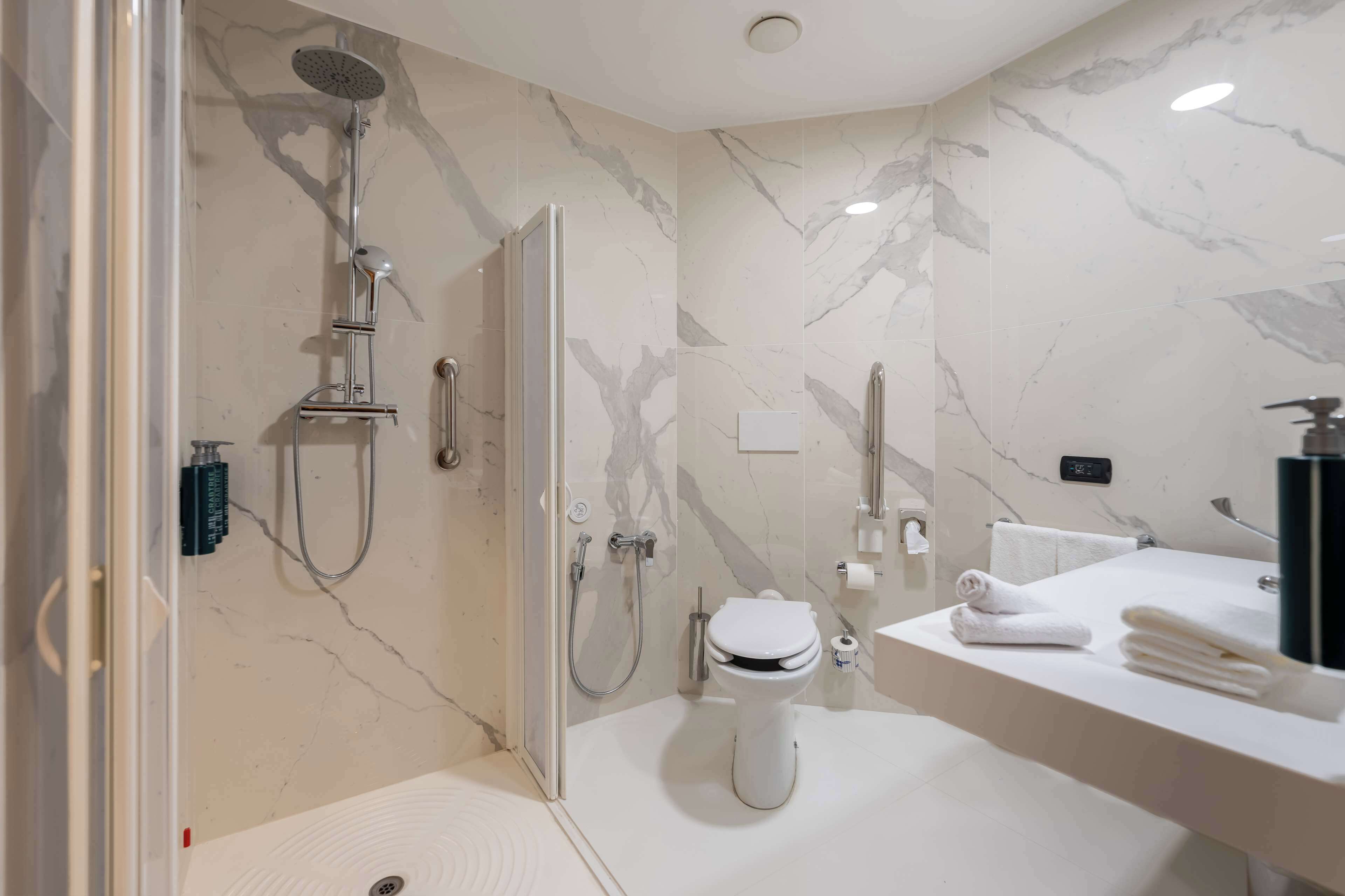 A modern bathroom with a shower, toilet, and sink, featuring marble walls and a glass-enclosed shower area.
