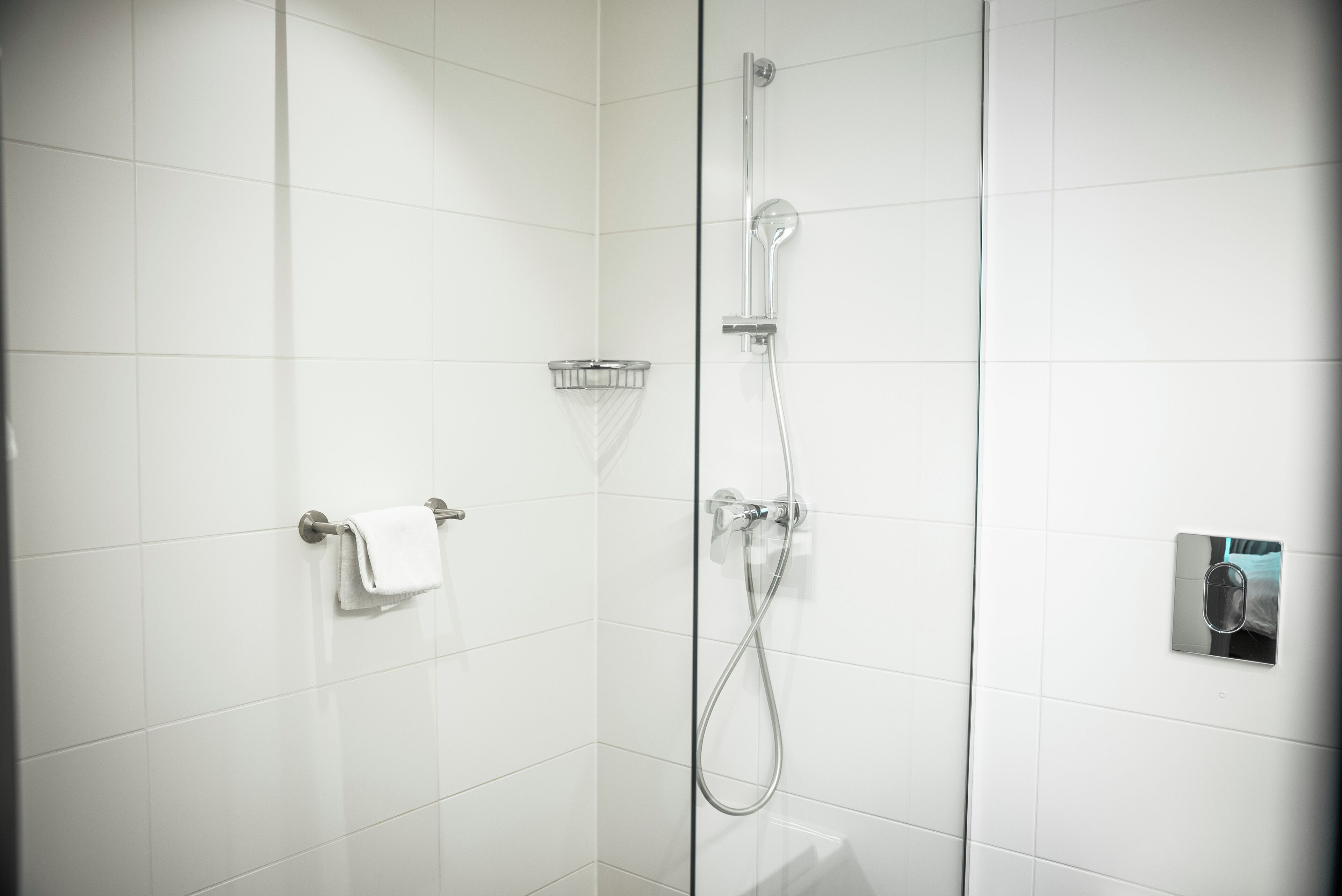 Un baño moderno con azulejos blancos, cabina de ducha de cristal, toallero y calentador de toallas integrado.