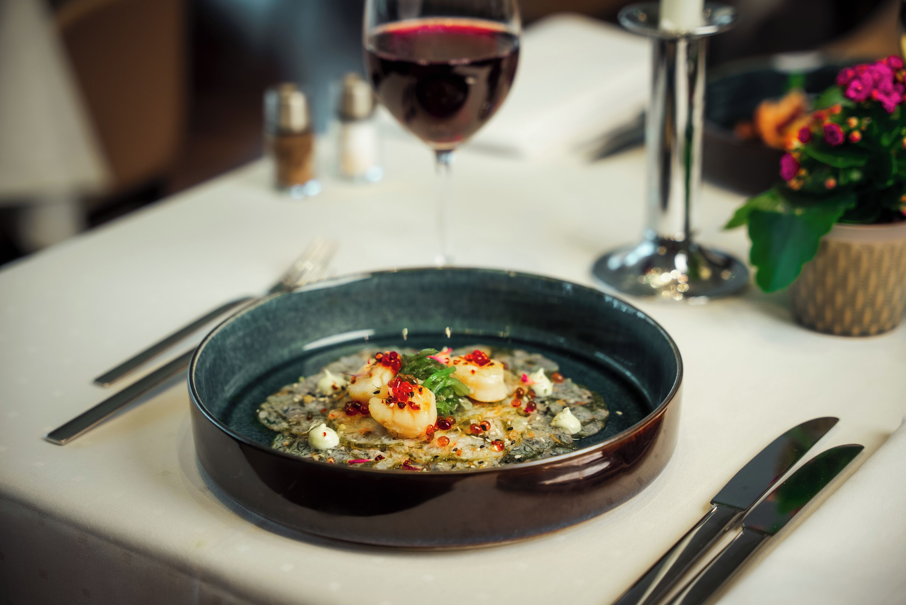 A bowl of seafood dish on a table with a wine glass and cutlery.