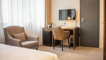 A hotel room with a bed, a desk with a computer, a chair, a television, and a minibar.