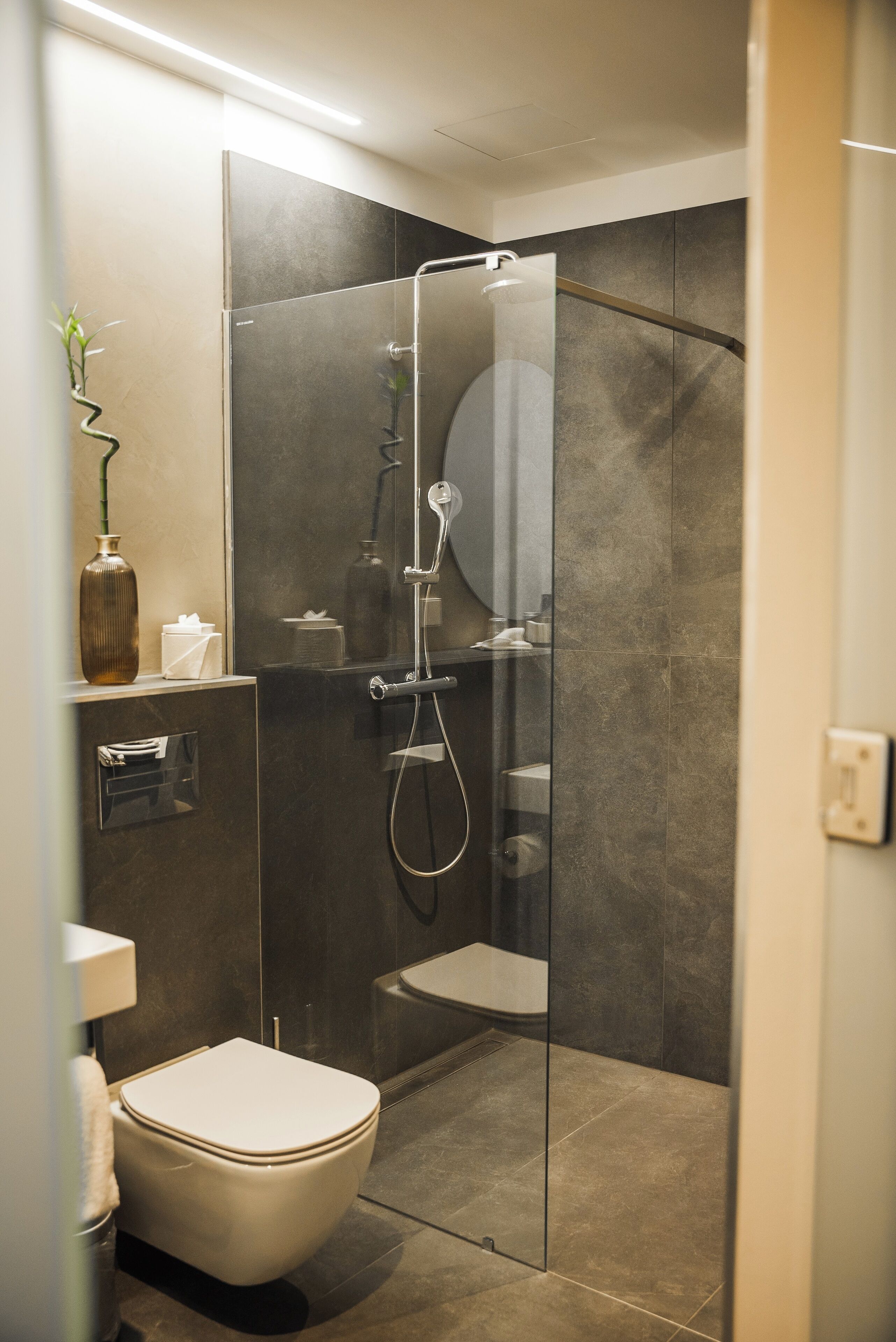 A modern bathroom with a glass-enclosed shower, a toilet, and a small shelf with a vase and tissues.
