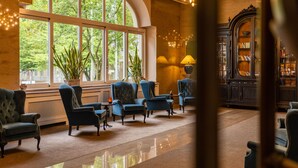 A lobby with large arched windows, a grand piano, and a library with bookshelves. - Parkhotel Kurhaus (Bad Kreuznach)