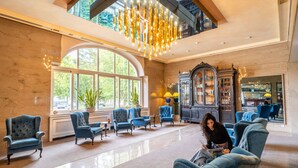 A spacious lobby with a high ceiling, large windows, and a grand piano. - Parkhotel Kurhaus (Bad Kreuznach)