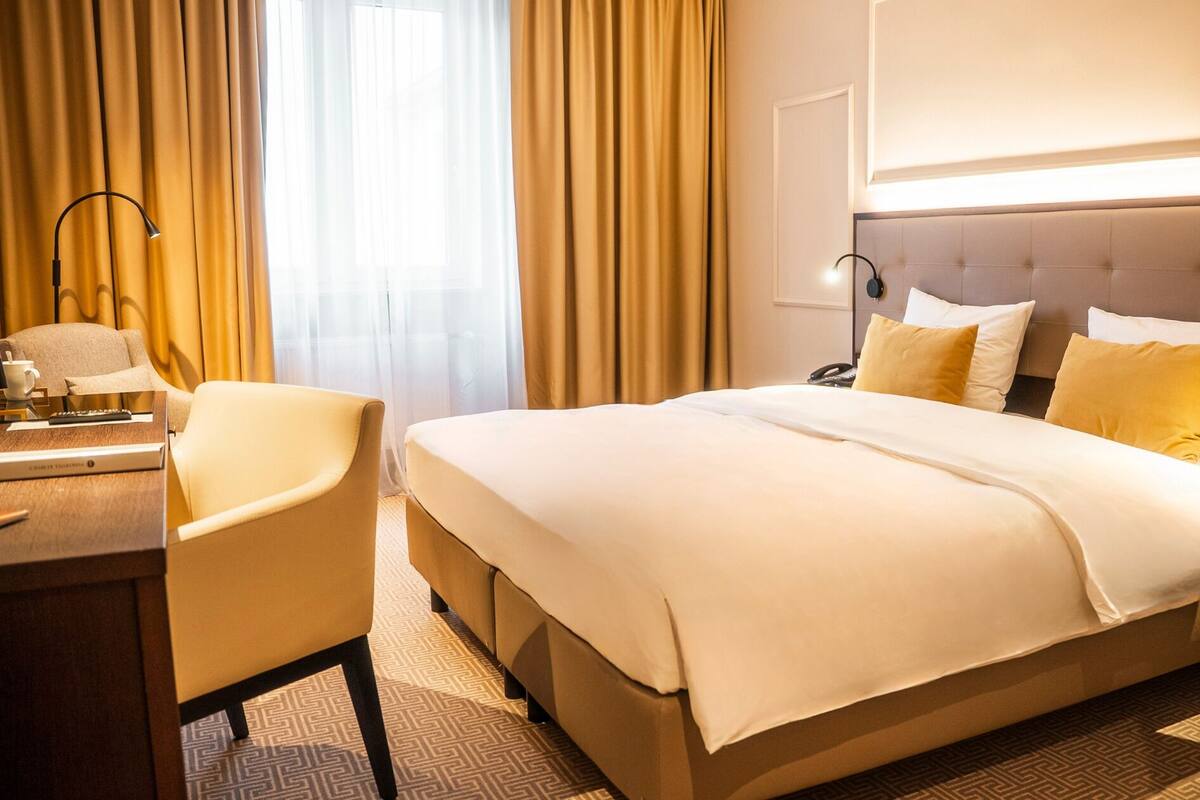 A hotel room with a large bed, a desk with a chair, and a lamp.
