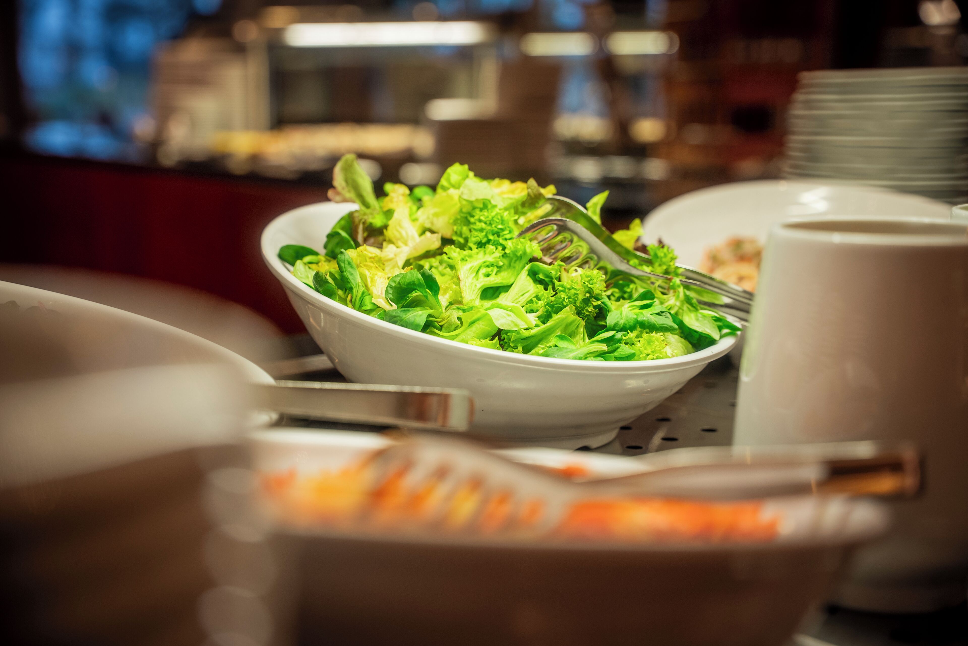 A dining table with a bowl of salad, a fork, and a cup.