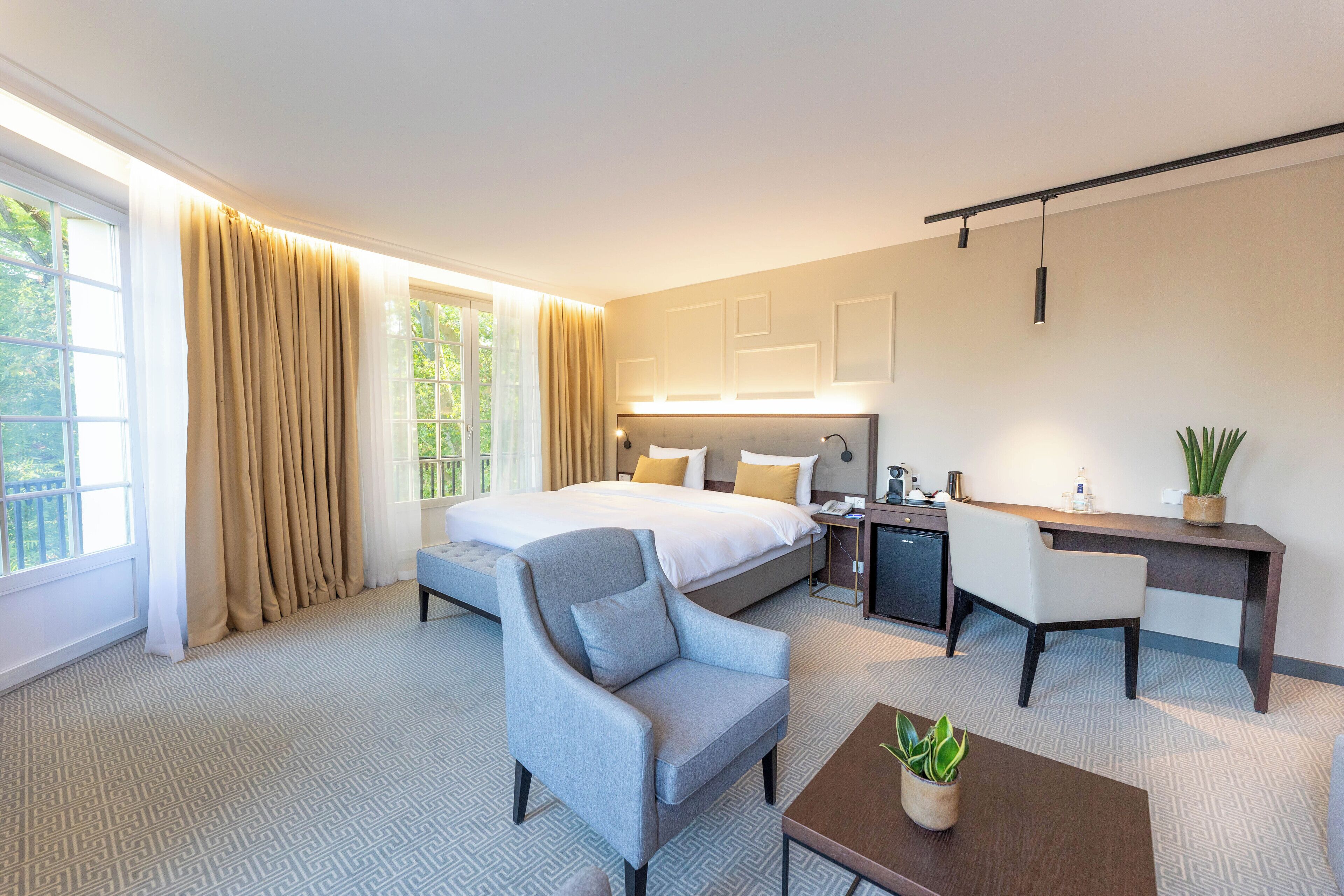 A hotel room with a bed, a desk, a chair, and a small table with a plant.