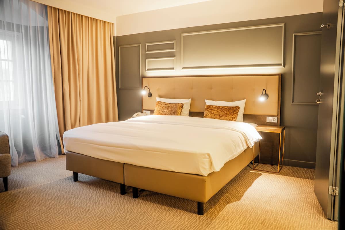 A hotel room with a large bed, a bedside table, a lamp, and a wardrobe.