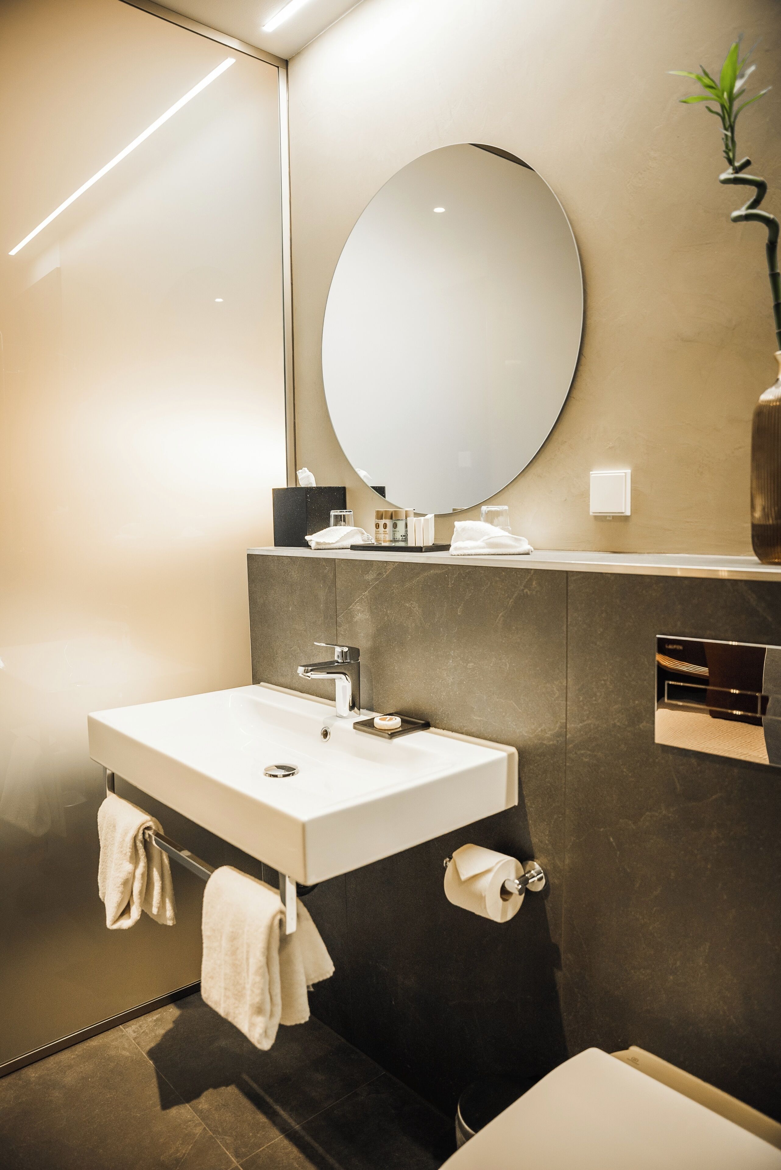 Un baño moderno con un espejo grande, un lavamanos blanco y un perchero para toallas.