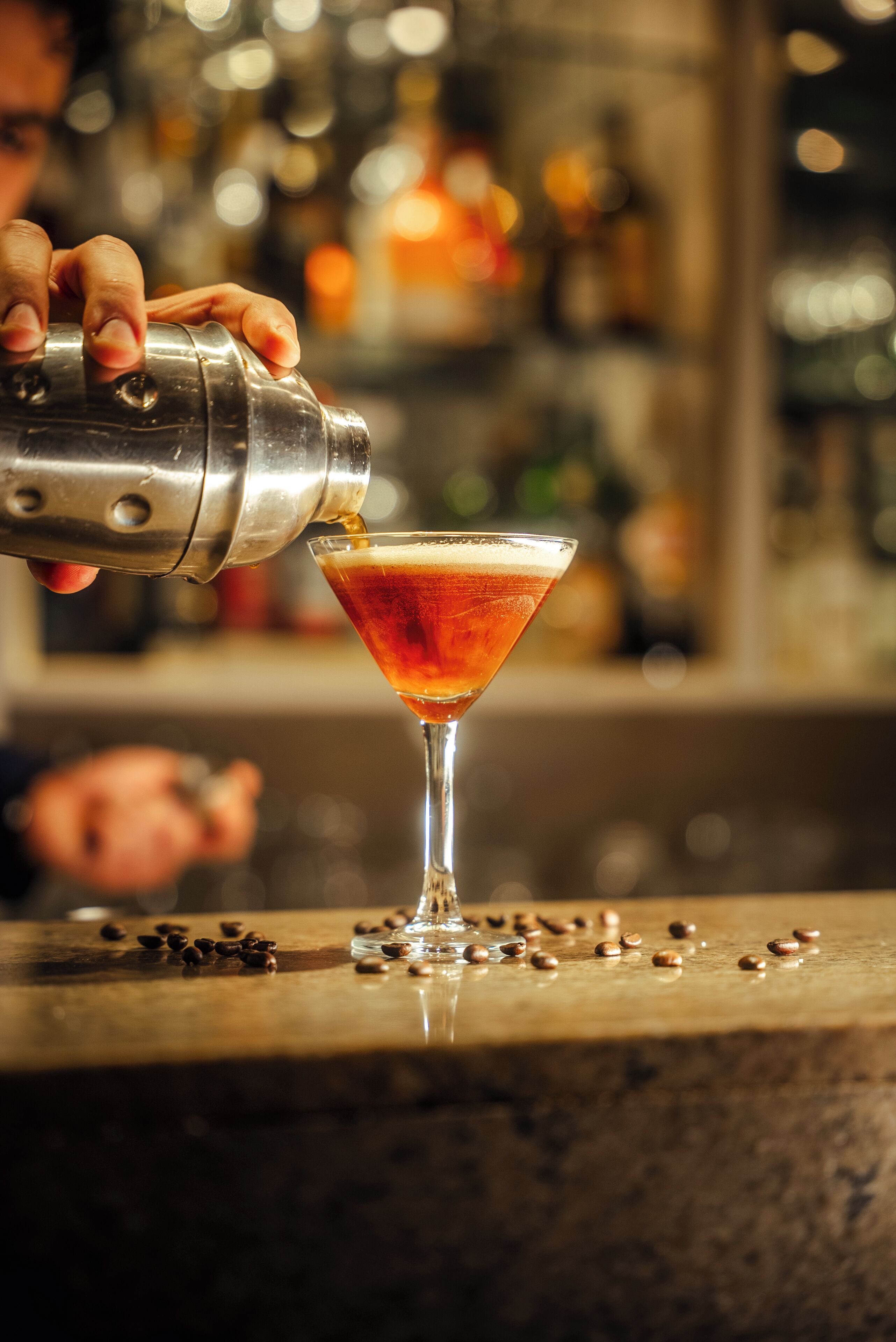 Ein Barkeeper gießt ein Getränk in ein Martini-Glas.