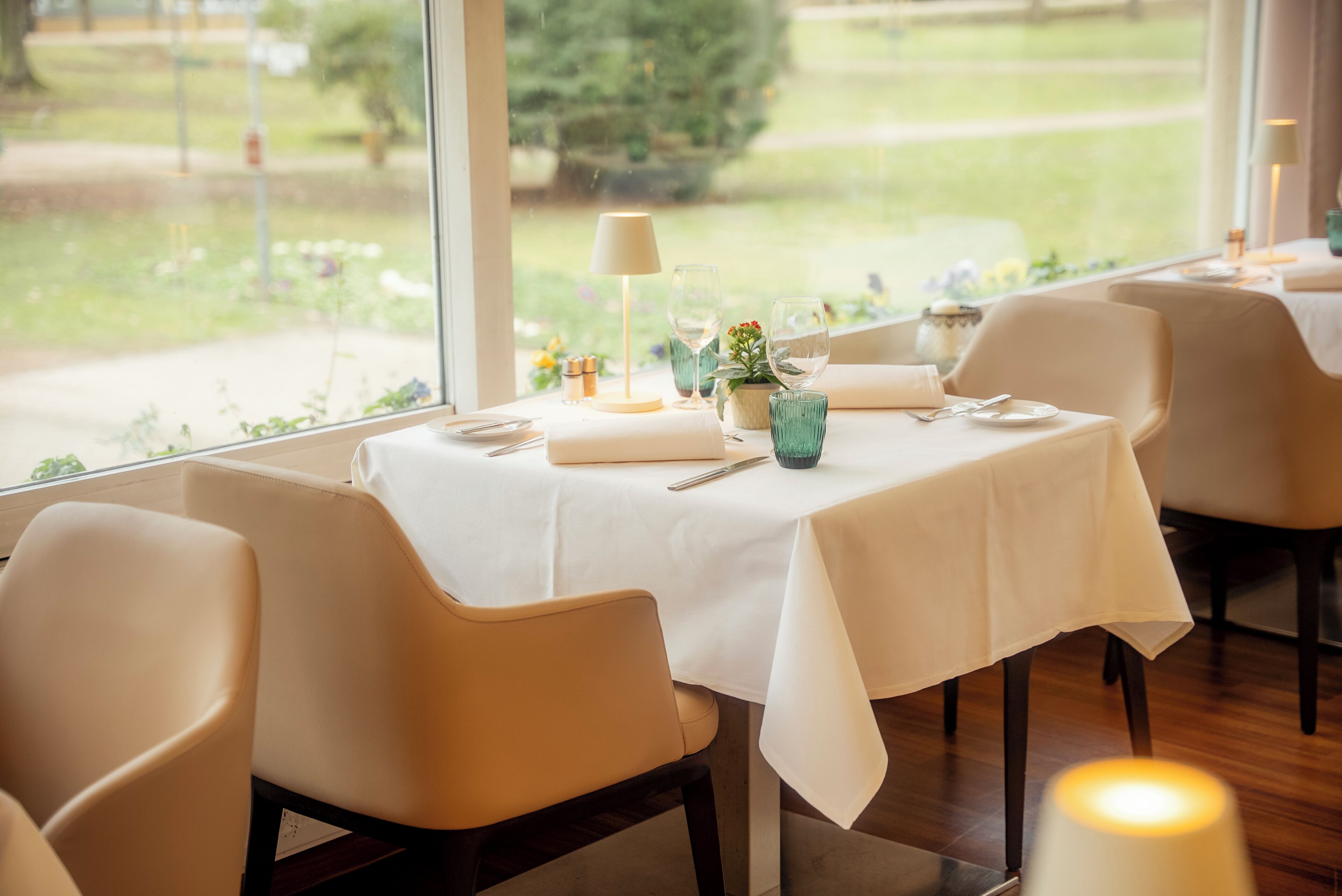 Comedor con mesas dispuestas para dos, con manteles blancos y vistas a un jardín a través de amplios ventanales.