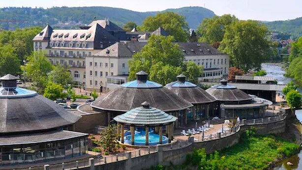 A riverside hotel with a circular building, a swimming pool, and a view of the river and hills in the background. - Parkhotel Kurhaus (Bad Kreuznach)