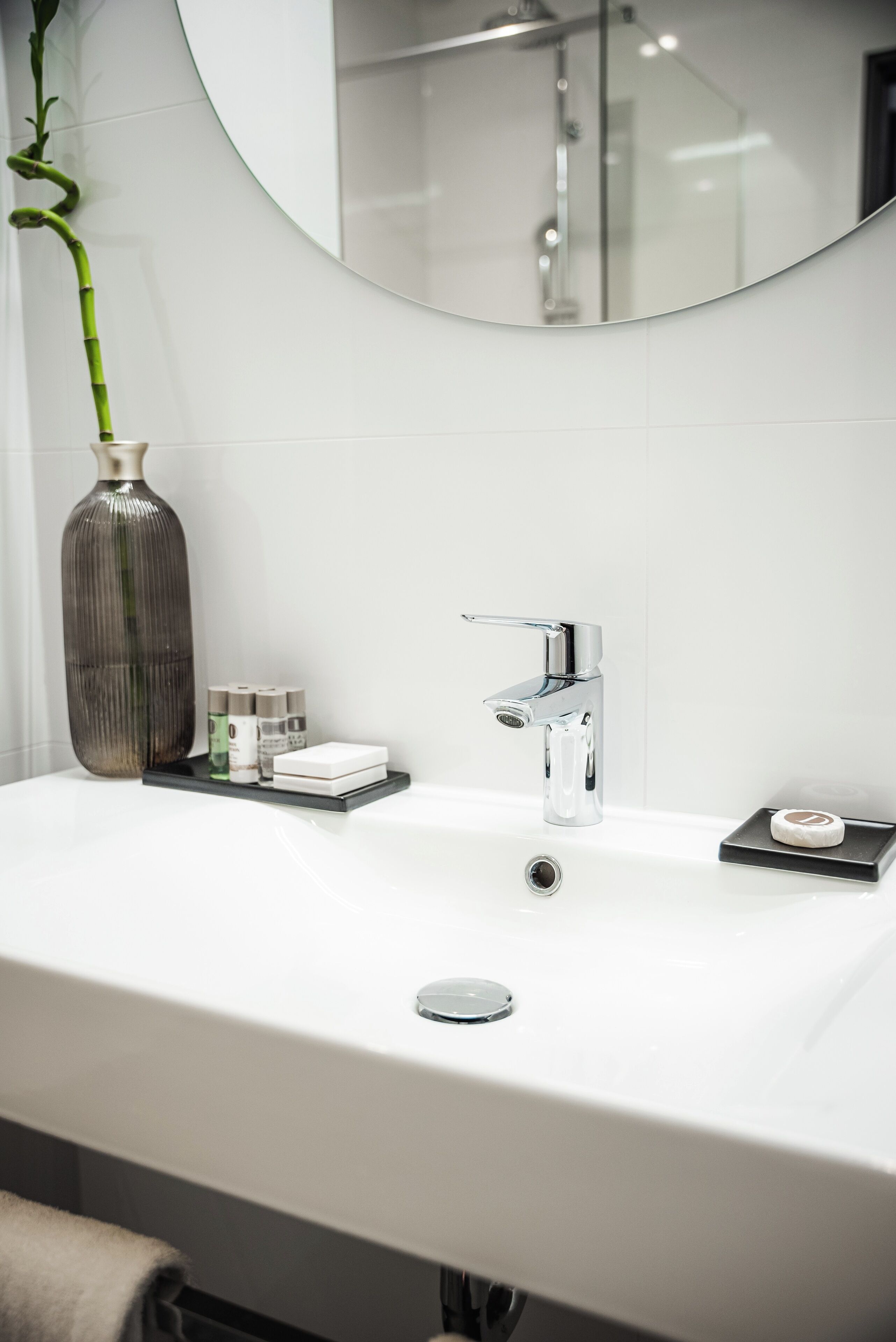 A modern bathroom with a white sink, chrome faucet, and a large mirror.