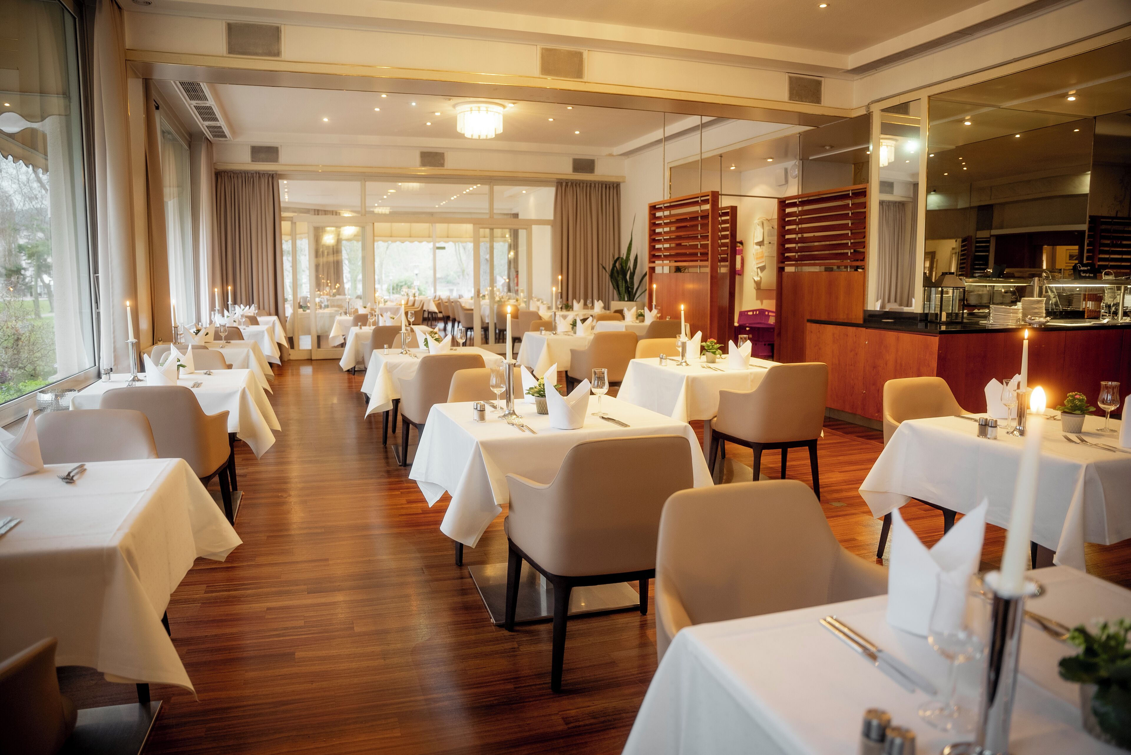 Un restaurante con varias mesas dispuestas para comer, con manteles blancos, velas y suelo de madera.