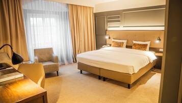 A hotel room with a large bed, a desk, a chair, and a nightstand with a lamp.